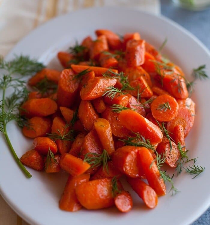 Roasted Carrots with dill on a white plate sitting on a yellow cloth napkin