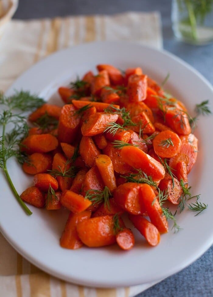 Roasted Carrots with dill on a white plate sitting on a yellow cloth napkin