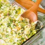 Traditional Seven Layer Salad in a clear glass baking dish with a wood spoon in it sitting on a white and green striped kitchen towel