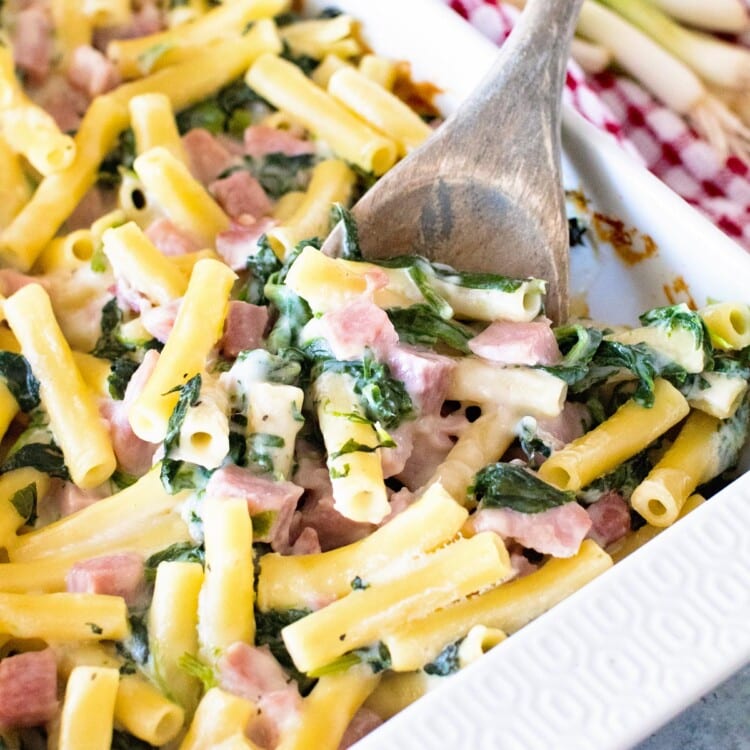 Spinach Ham Pasta Casserole in a white baking dish with a wood spoon in it