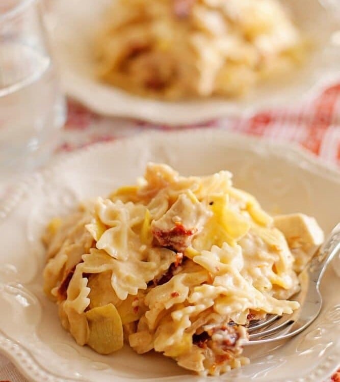 Two white plates of sun dried tomato and artichoke pasta with forks