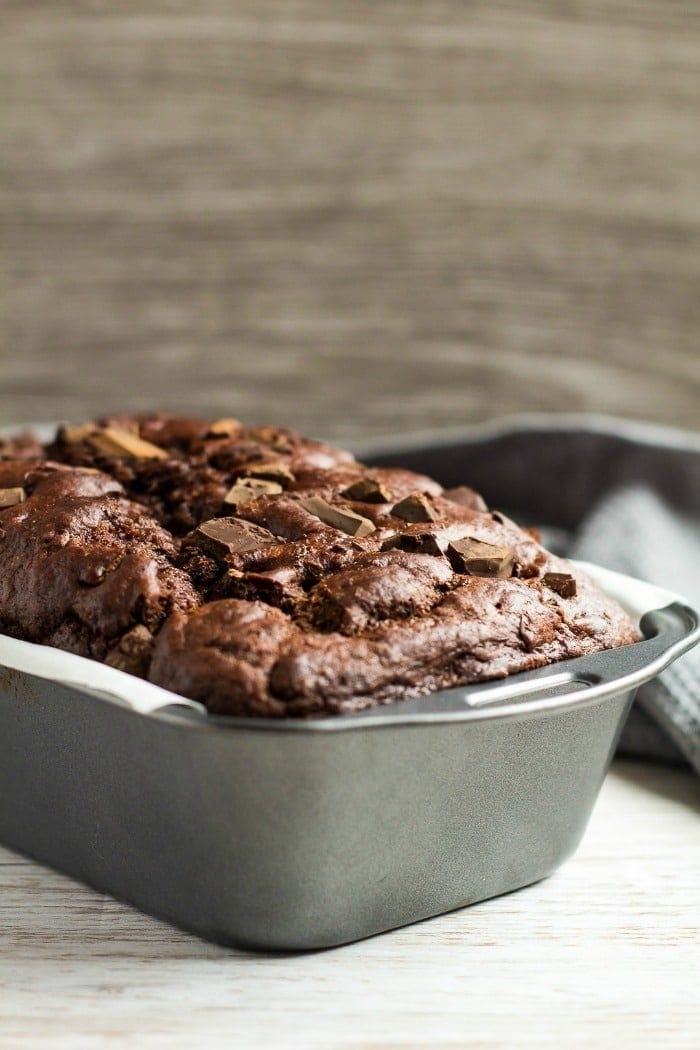 Metal loaf pan with parchment paper over edges and chocolate banana bread in it