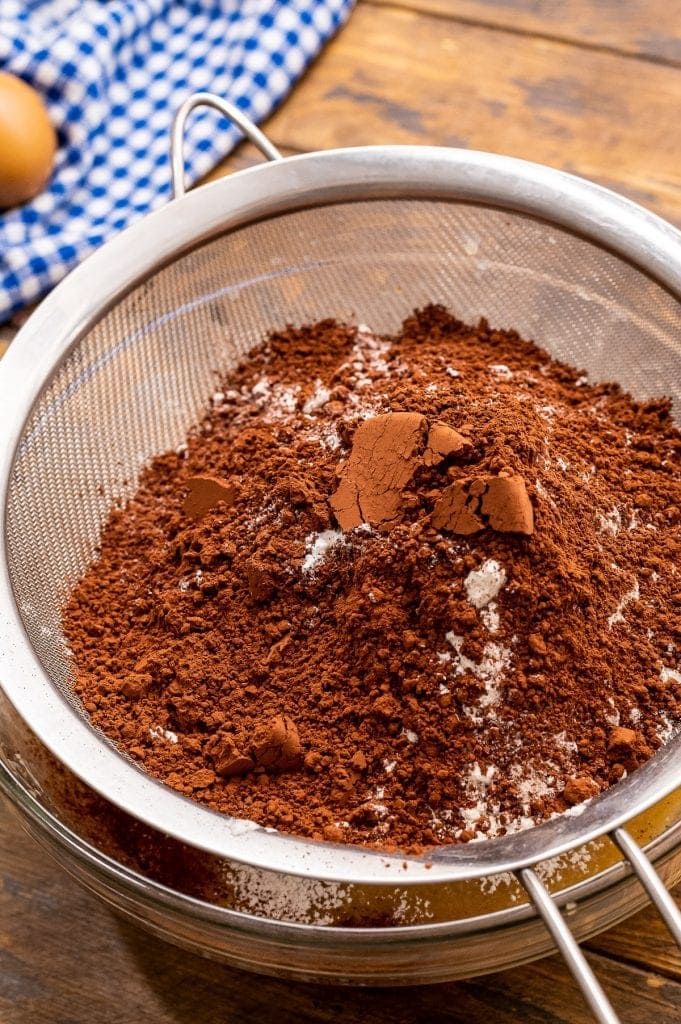 Sifting ingredients including cocoa powder in a mesh sieve. 