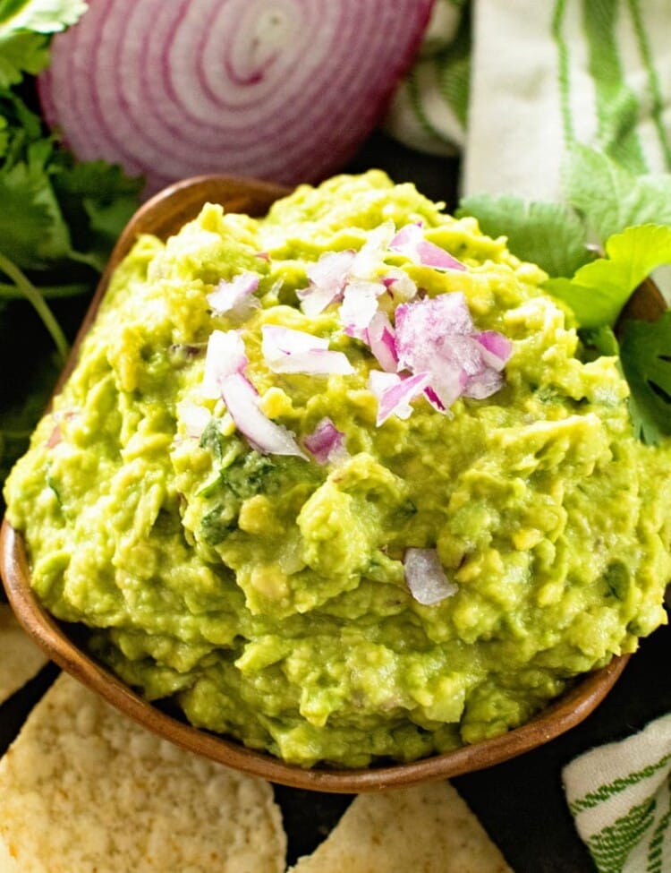 Homemade Guacamole in bowl next to an onion and tortilla chips