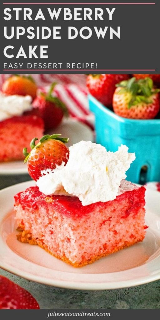 Strawberry Upside Down Cake topped with whipped cream and a strawberry on a white plate with a blue crate of strawberries in the background