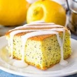 Poppy seed cake piece on a white plate with lemons and eggs in the background