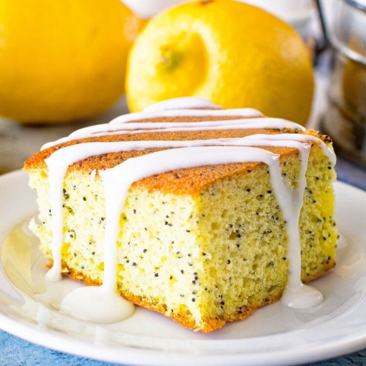 Poppy seed cake piece on a white plate with lemons and eggs in the background