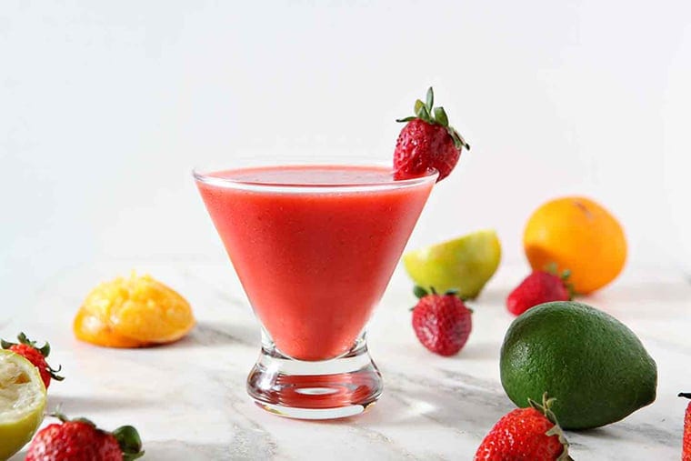 A Strawberry Virgin Margarita sits on a marble background, surrounded by strawberries, limes and oranges.
