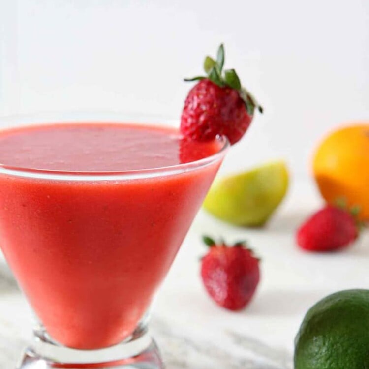 A Strawberry Virgin Margarita sits on a marble background, surrounded by strawberries, limes and oranges.