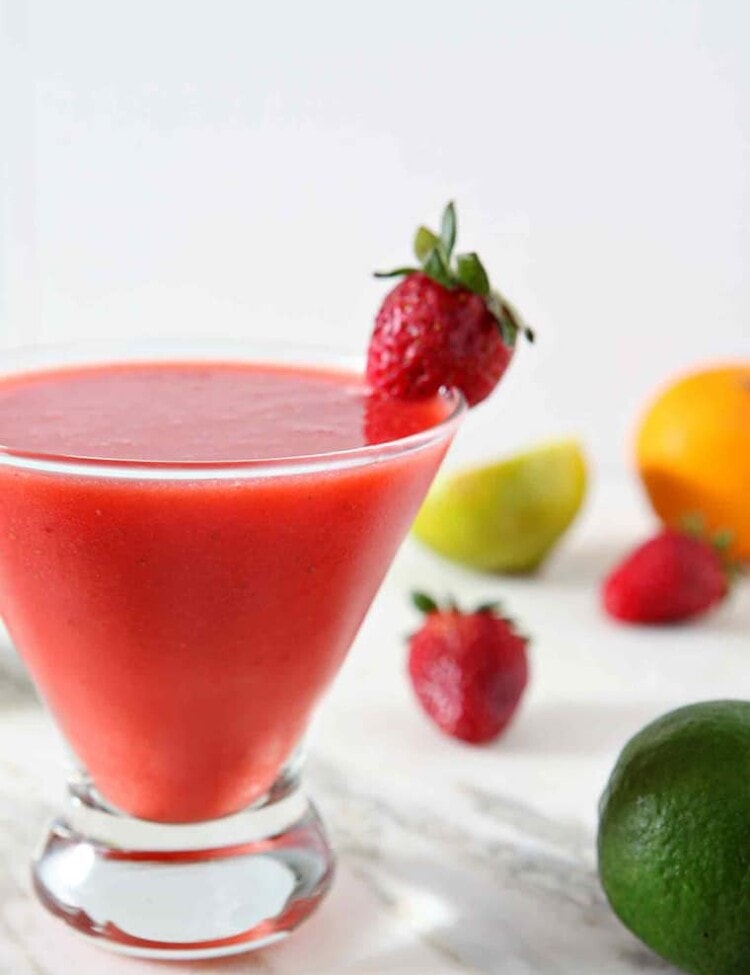 A Strawberry Virgin Margarita sits on a marble background, surrounded by strawberries, limes and oranges.