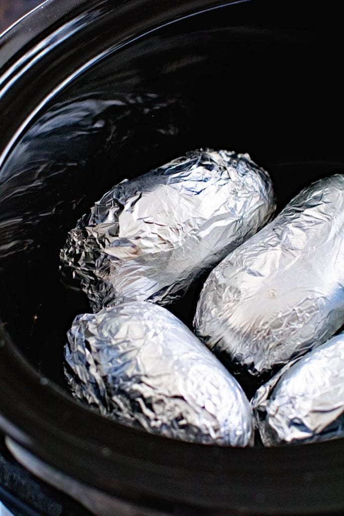 Potatoes wrapped in aluminum foil in a black crock pot