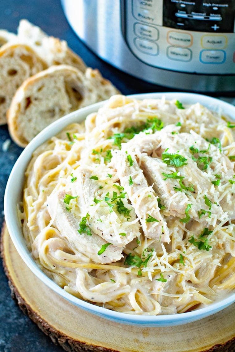 Chicken alfredo in white bowl topped with chopped parsley with an Instant Pot in background.