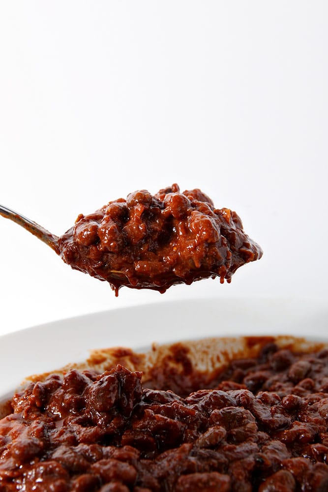 A spoon scoops out a serving of Pressure Cooker Baked Beans from a white bowl