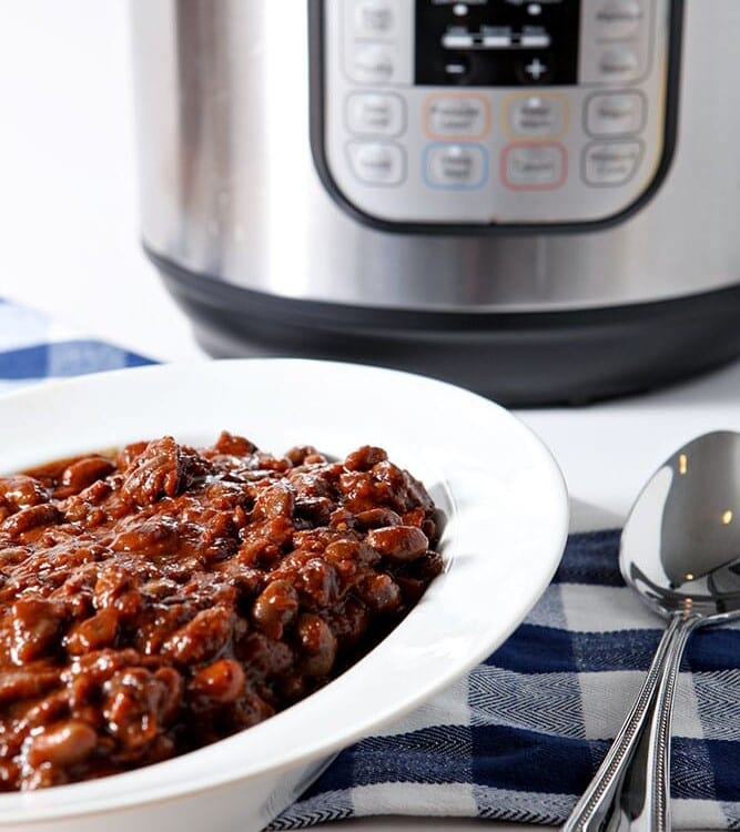 Instant Pot Baked Beans are served in a white bowl in front of an Instant Pot