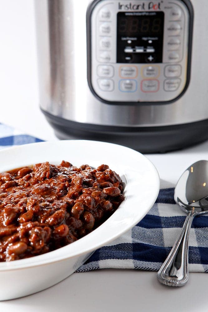Instant Pot Baked Beans are served in a white bowl in front of an Instant Pot