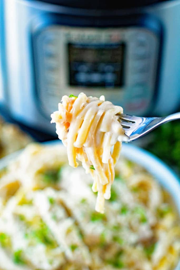 A fork with chicken alfredo on it and a bowl of alfredo and an Instant Pot in background.