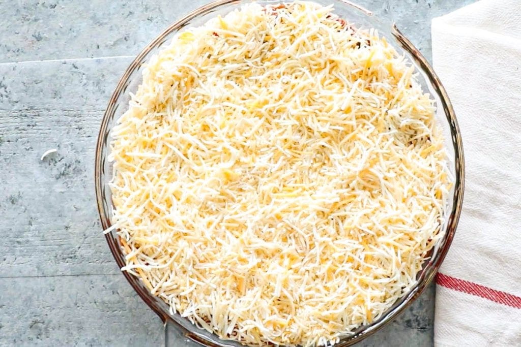 Glass pie dish with final layer of shredded cheese
