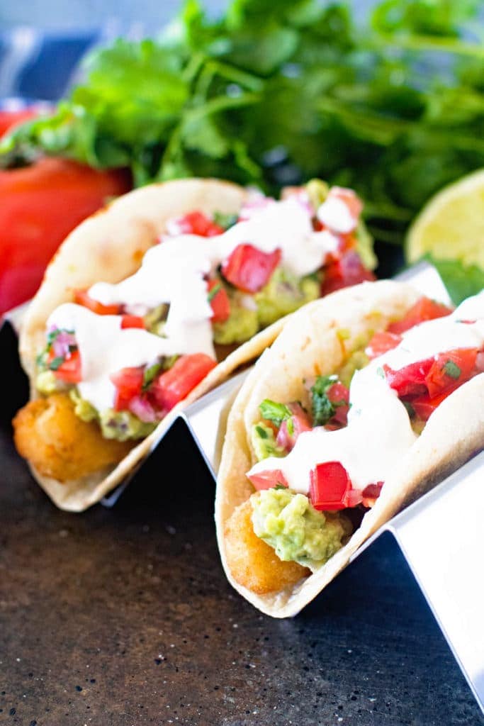 Metal stand holding tacos with cilantro tomato and limes in background