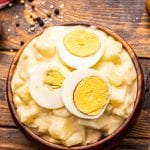 Overhead photo of brown bowl with potato salad and sliced eggs on top
