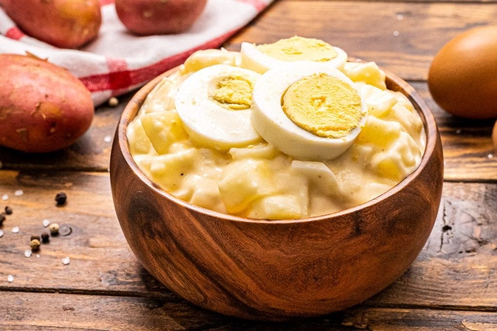 Side view photo of a wooden bowl with potato salad topped with hardboiled eggs.