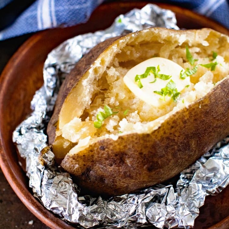 Baked Potato with butter in foil on a wood plate