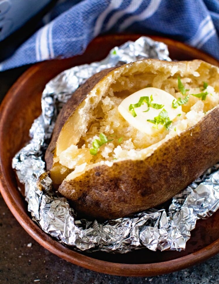 Baked Potato with butter in foil on a wood plate