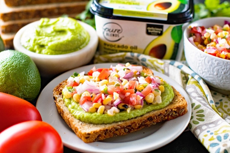 Avocado Butter toast on white plate topped with grilled corn salsa