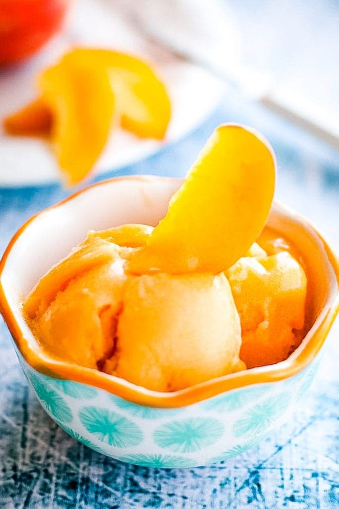 Blue background with bowl of peach sorbet garnished with fresh peach