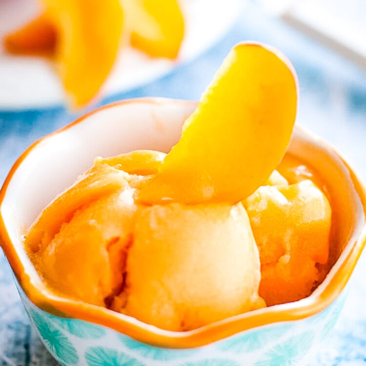 Blue background with bowl of peach sorbet garnished with fresh peach