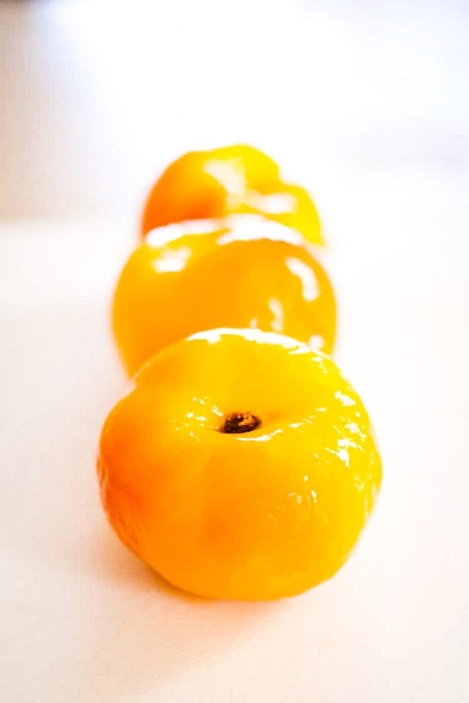 Peeled peaches lined up in a row on white background