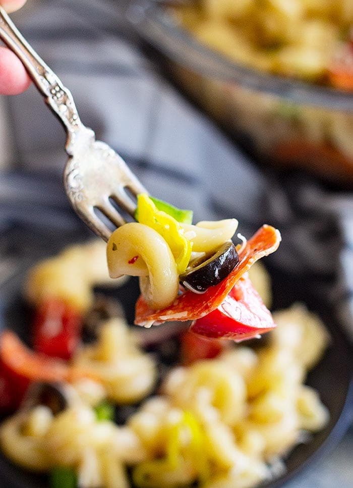 Pepperoni Pasta Salad on Fork with a bowl of Pasta Salad with Pepperoni in the background.