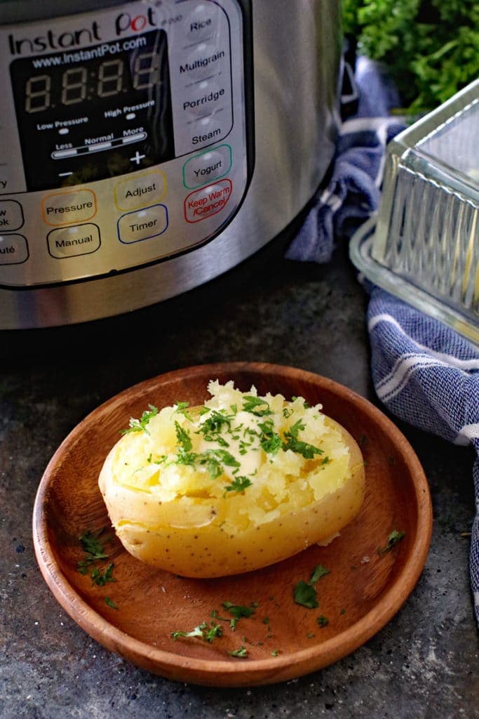 Cooked Potato on brown plate with an Instant pot, dish of butter and blue and white napkin in background