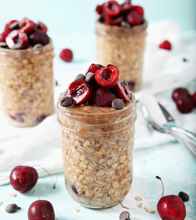 Three jars of Cherry Overnight Oats sit on a white towel, ready for serving