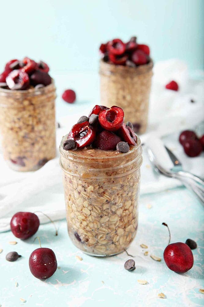 Three jars of Cherry Overnight Oats sit on a white towel, ready for serving