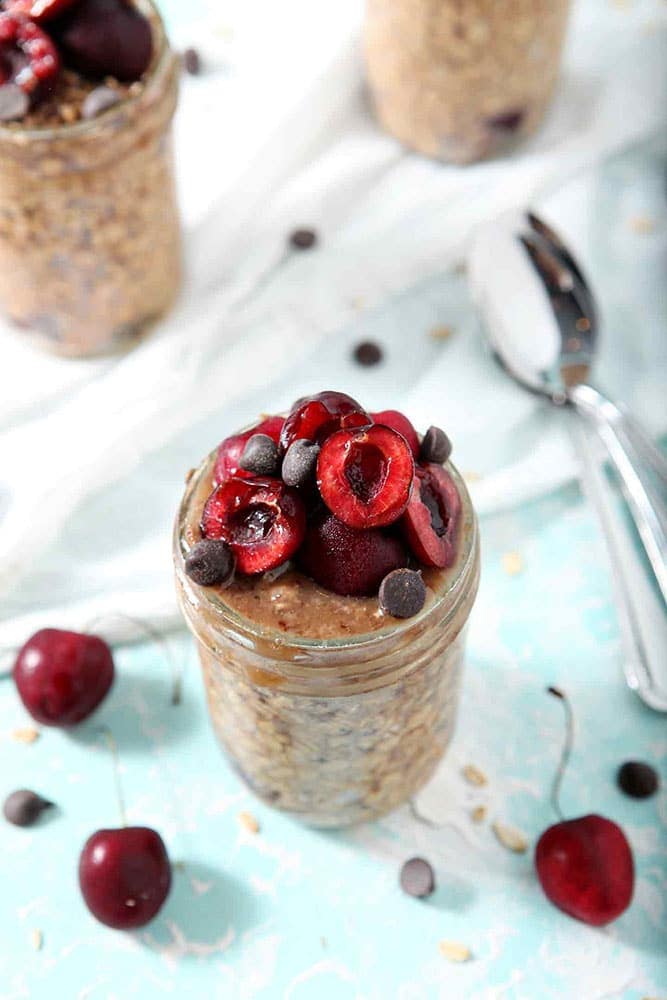Closer look at three jars of Cherry Overnight Oats sit on a white towel, ready for serving