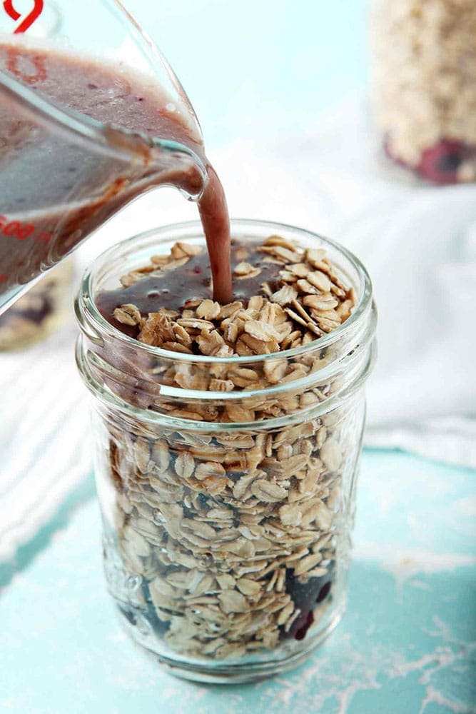 How to make overnight oats - A mixture of cashew milk, maple syrup and cherry puree are poured in top of rolled oats