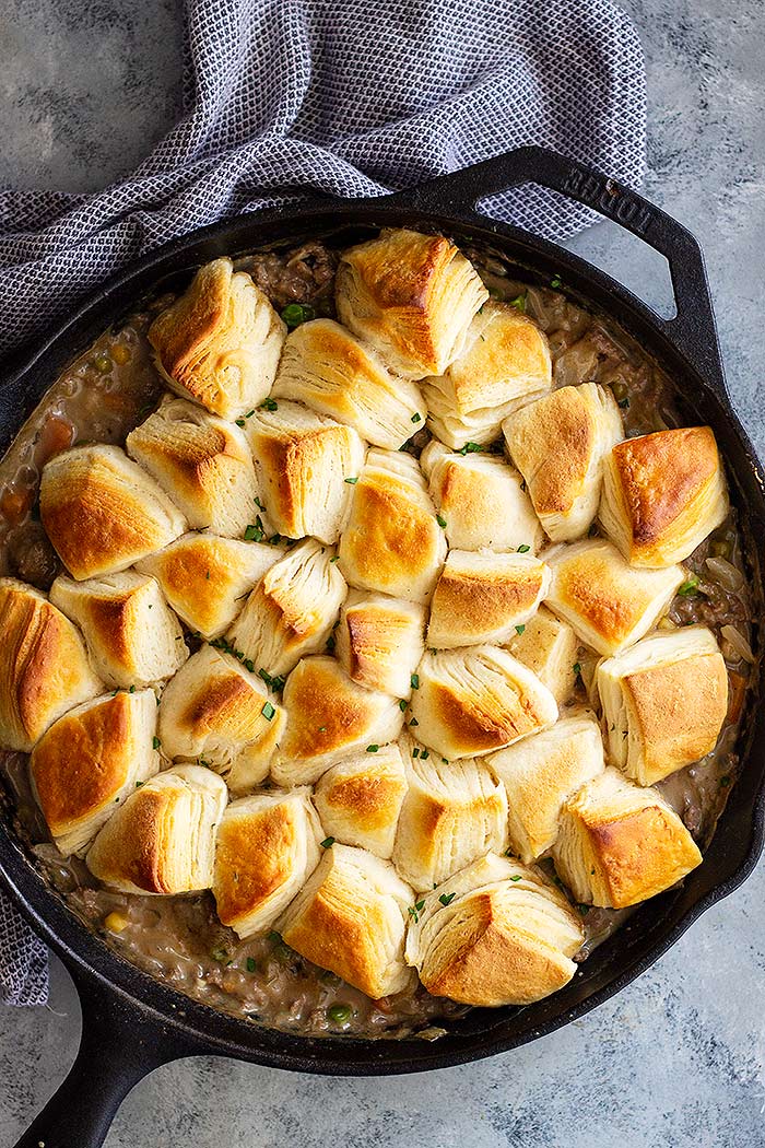 A cast iron skillet filled with beef pot pie topped with biscuits.