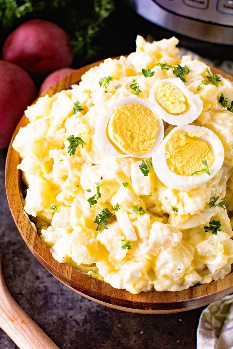 Wooden bowl full of potato salad garnished with chopped parsley and a sliced hard boiled egg. 