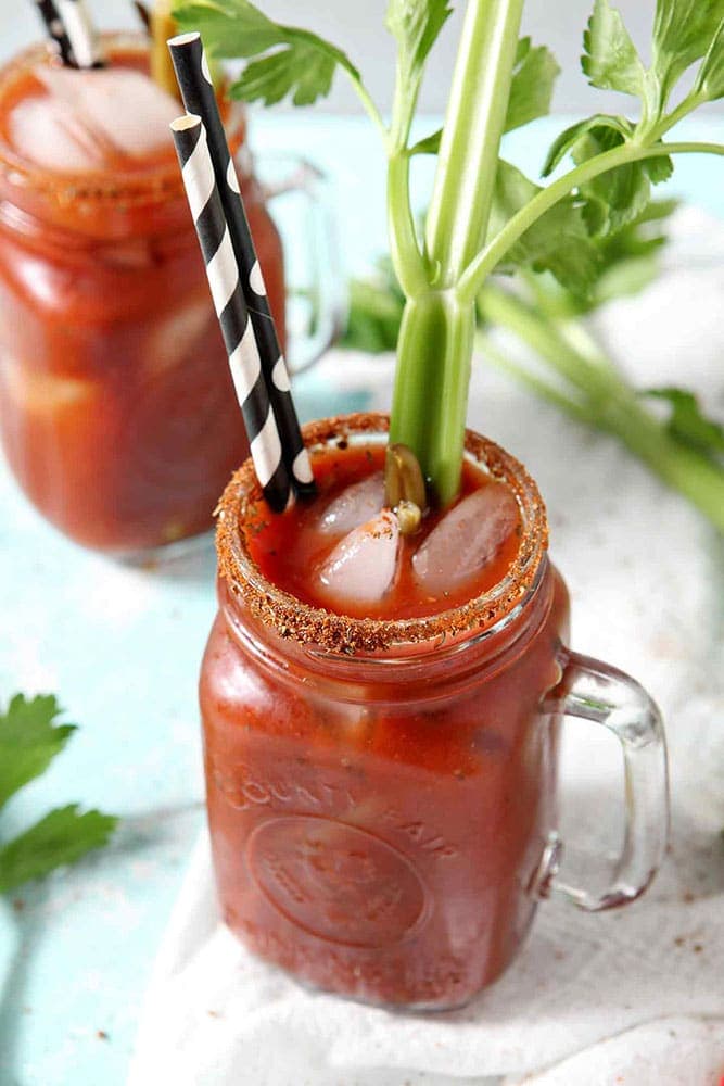 Two BBQ Bloody Marys are garnished with pickled green beans and fresh celery sticks