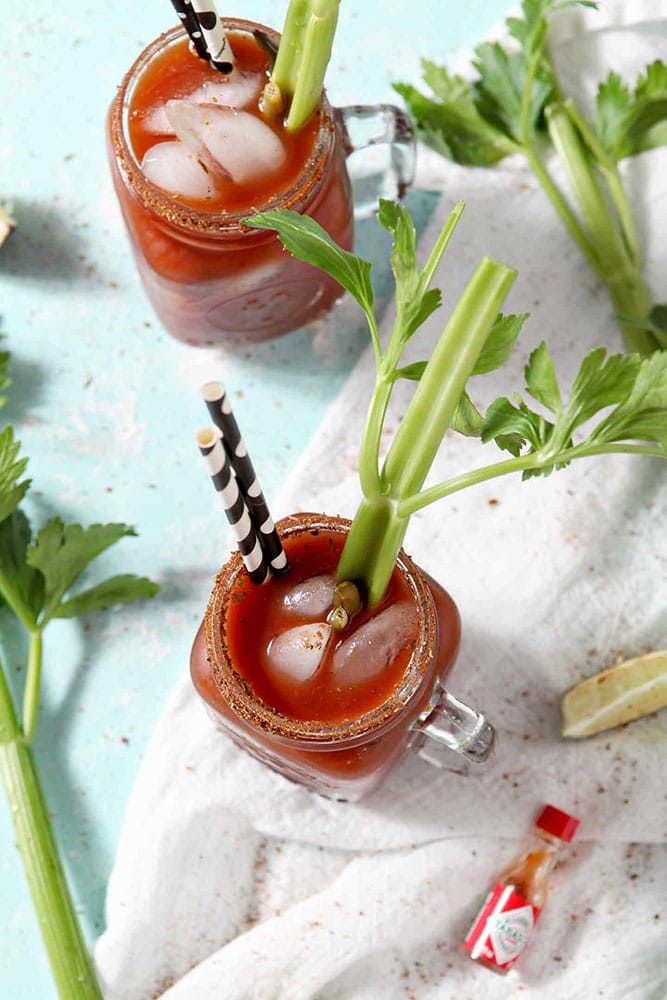 Two BBQ Bloody Marys are garnished with pickled green beans and fresh celery sticks