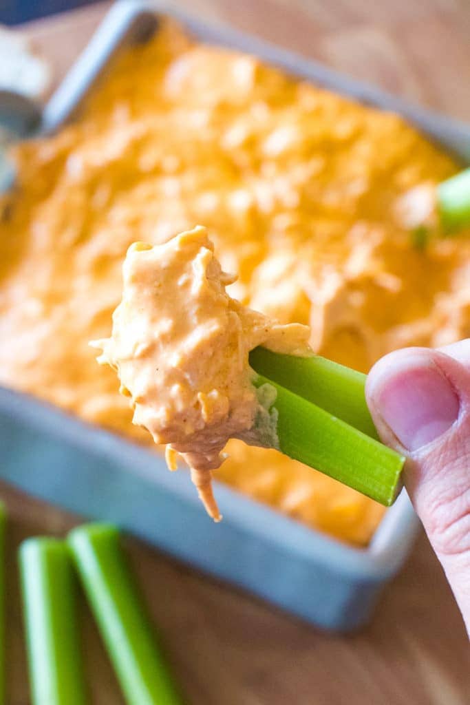 Piece of celery with a scoop of dip on it with a hand holding it