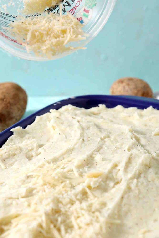 Parmesan cheese is sprinkled onto Garlic Parmesan Mashed Potato Casserole before the casserole goes into the oven