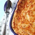 A close up of Garlic Parmesan Mashed Potato Casserole, shown in a purple baking dish with a serving spoon