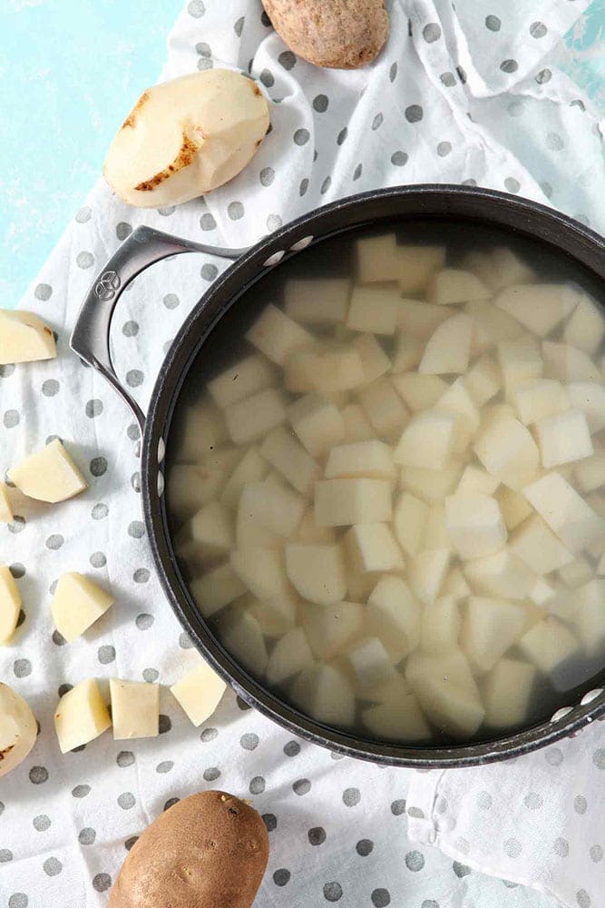 Chopped potatoes are shown in a pot, surrounded by other potatoes, before Garlic Parmesan Mashed Potato Casserole is made.