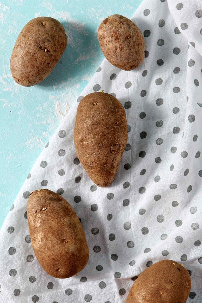 Potatoes are shown sitting on a grey polka dot towel on an aqua background