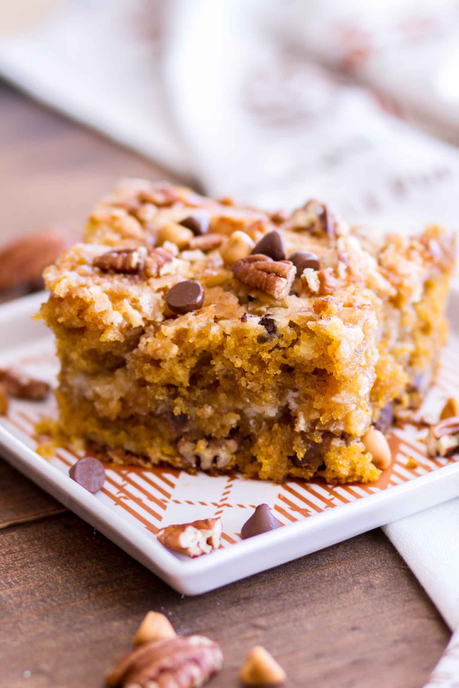 A serving of Pumpkin Earthquake Cake on a dish topped with chocolate and butterscotch chips and pecans.