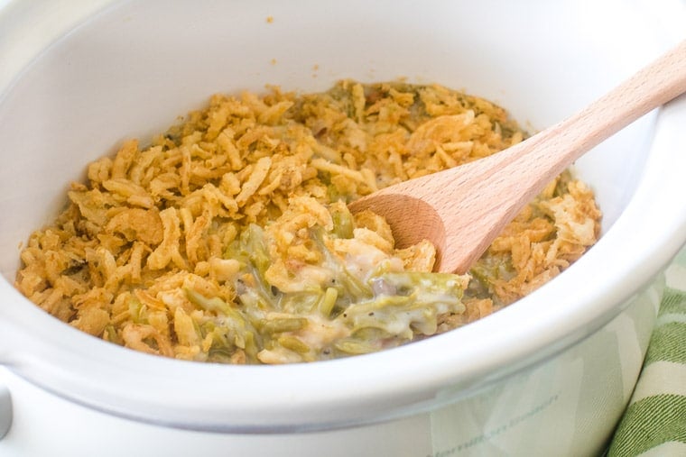 Wooden spoon in green bean casserole in a white crockpot