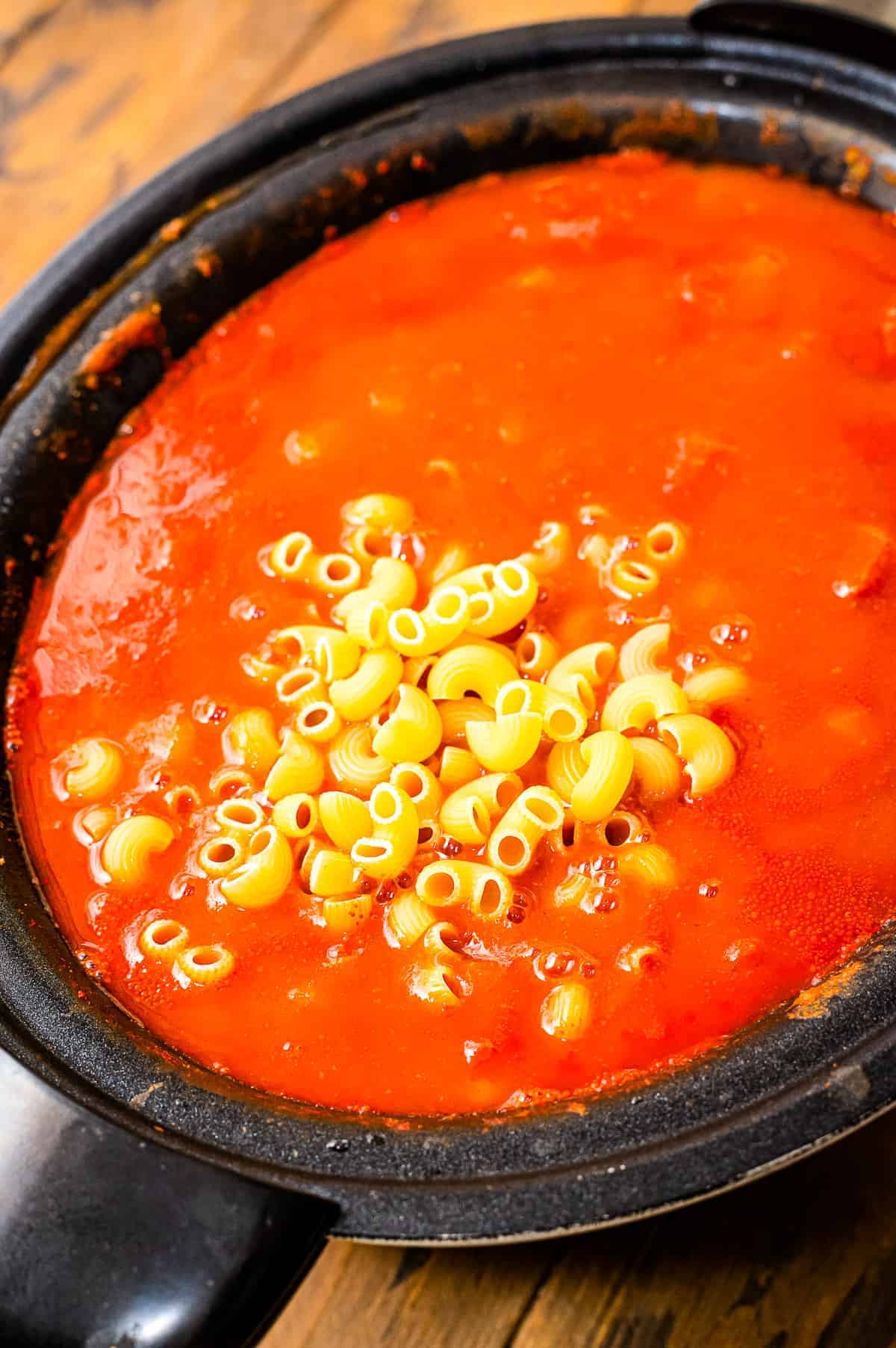 Slow cooker with elbow macaroni being added to chili