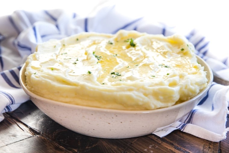 White speckled bowl with mashed potatoes butter on top and striped blue and white napkin in background