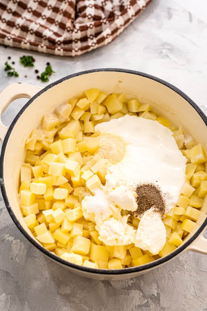 Dutch oven with cooked diced potatoes and ingredients to make mashed potatoes